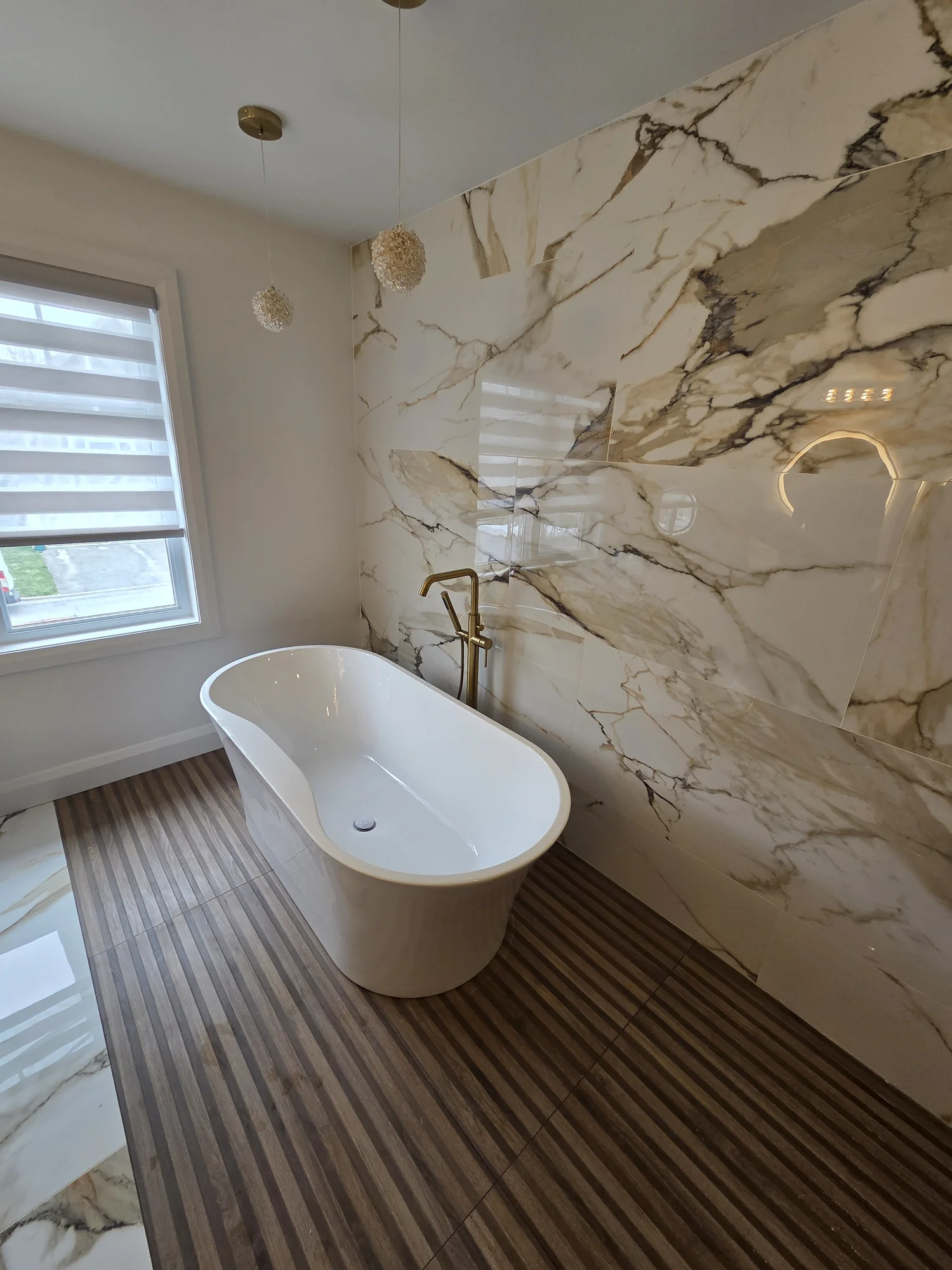 Freestanding bathtub beside a marble-effect feature wall