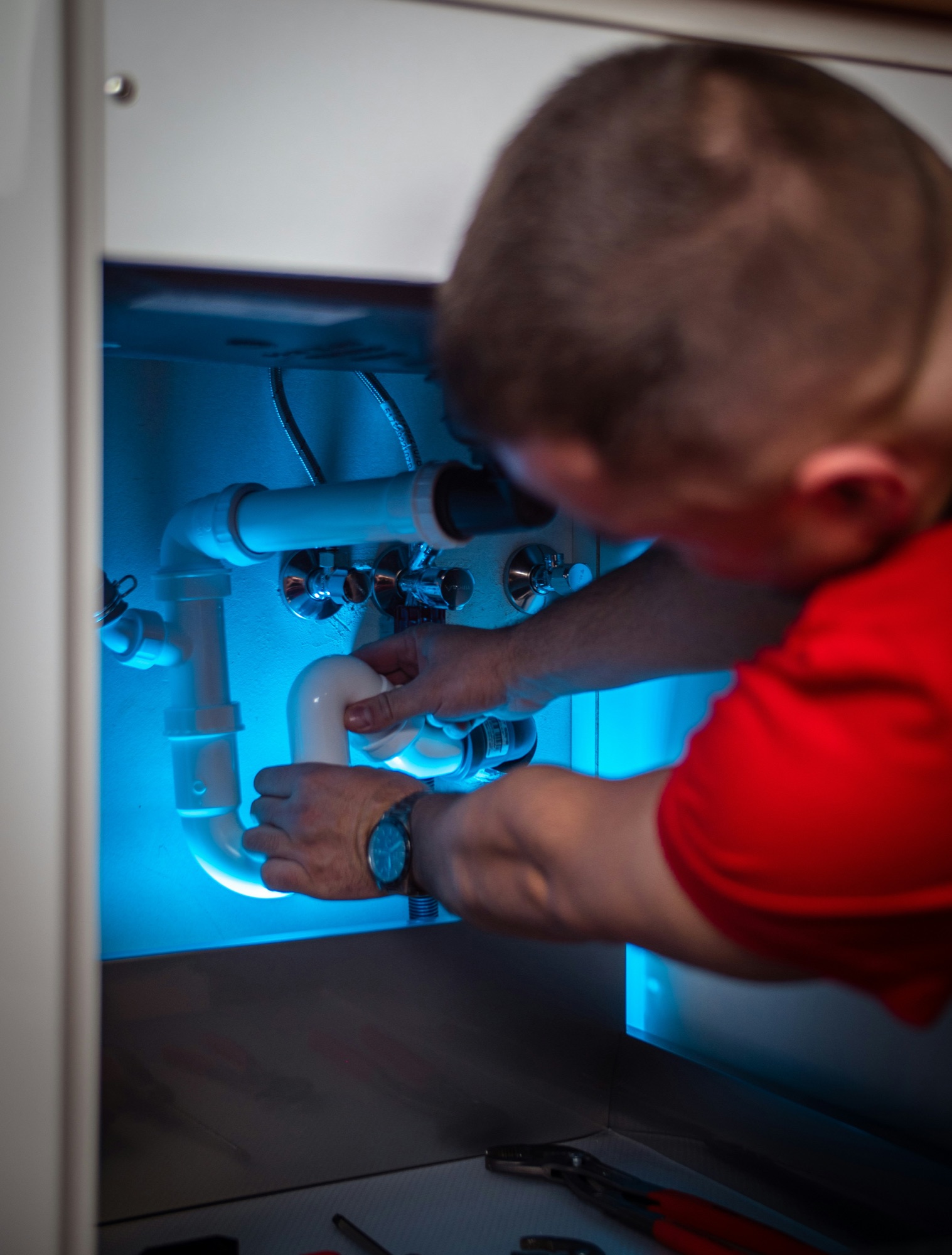A plumber repairing water and drain piping beneath a kitchen sink