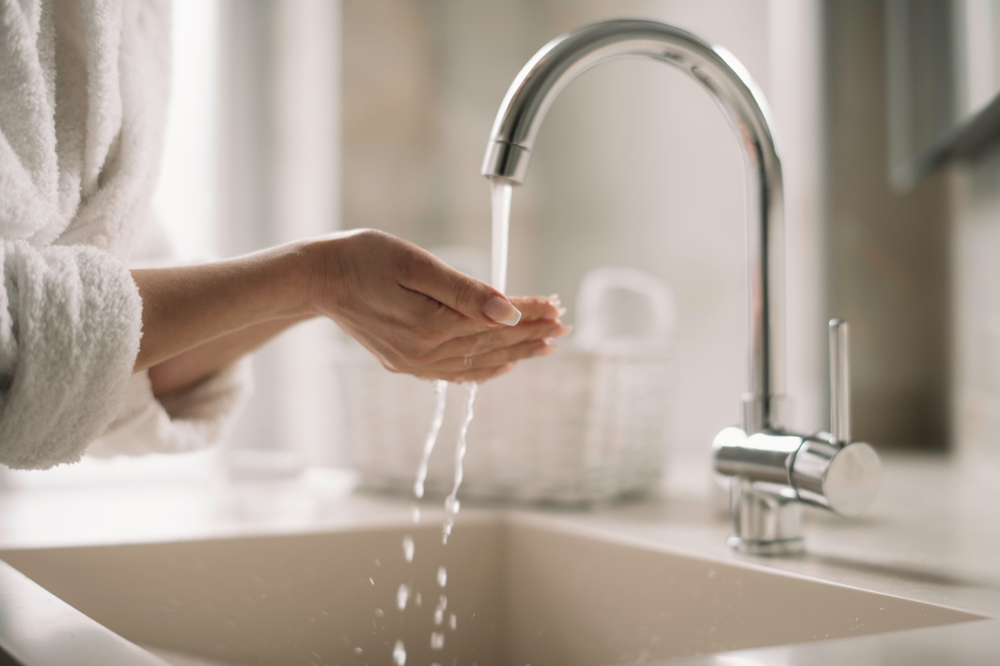 Hands beneath running water from a modern bathroom faucet