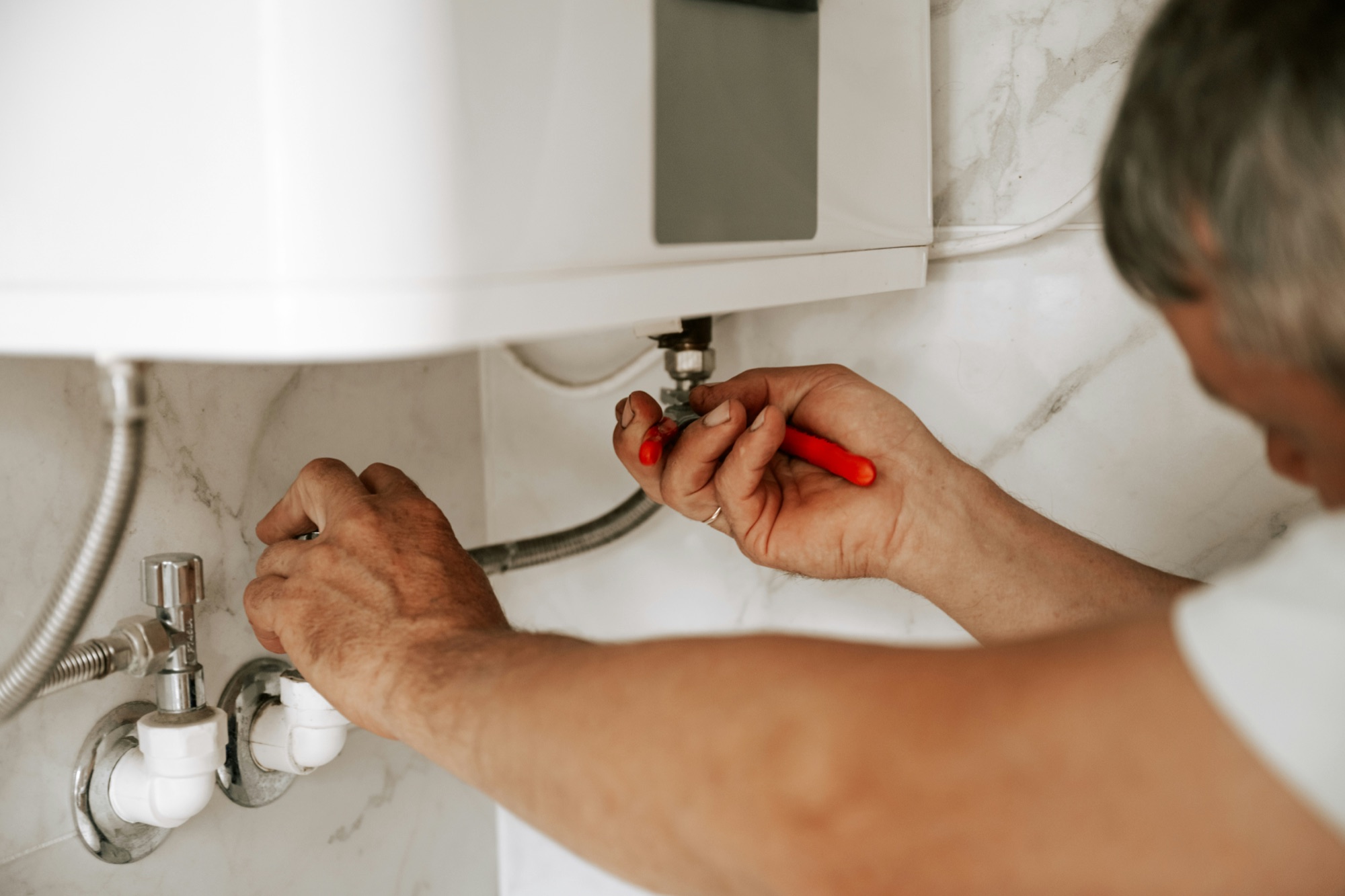 A plumber repairing faucet water lines beneath a sink