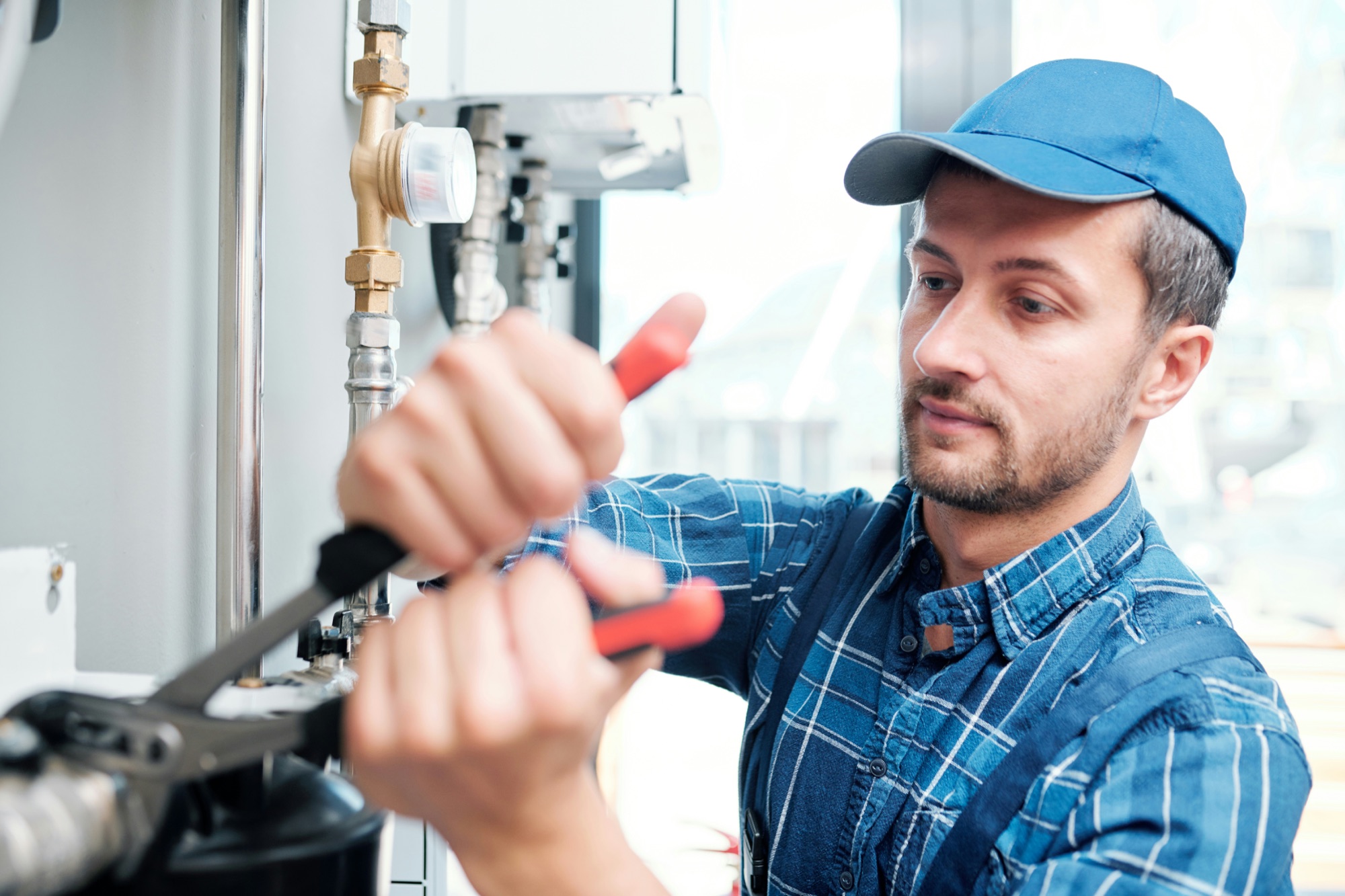 Plumber adjusting a valve beside hot-water equipment